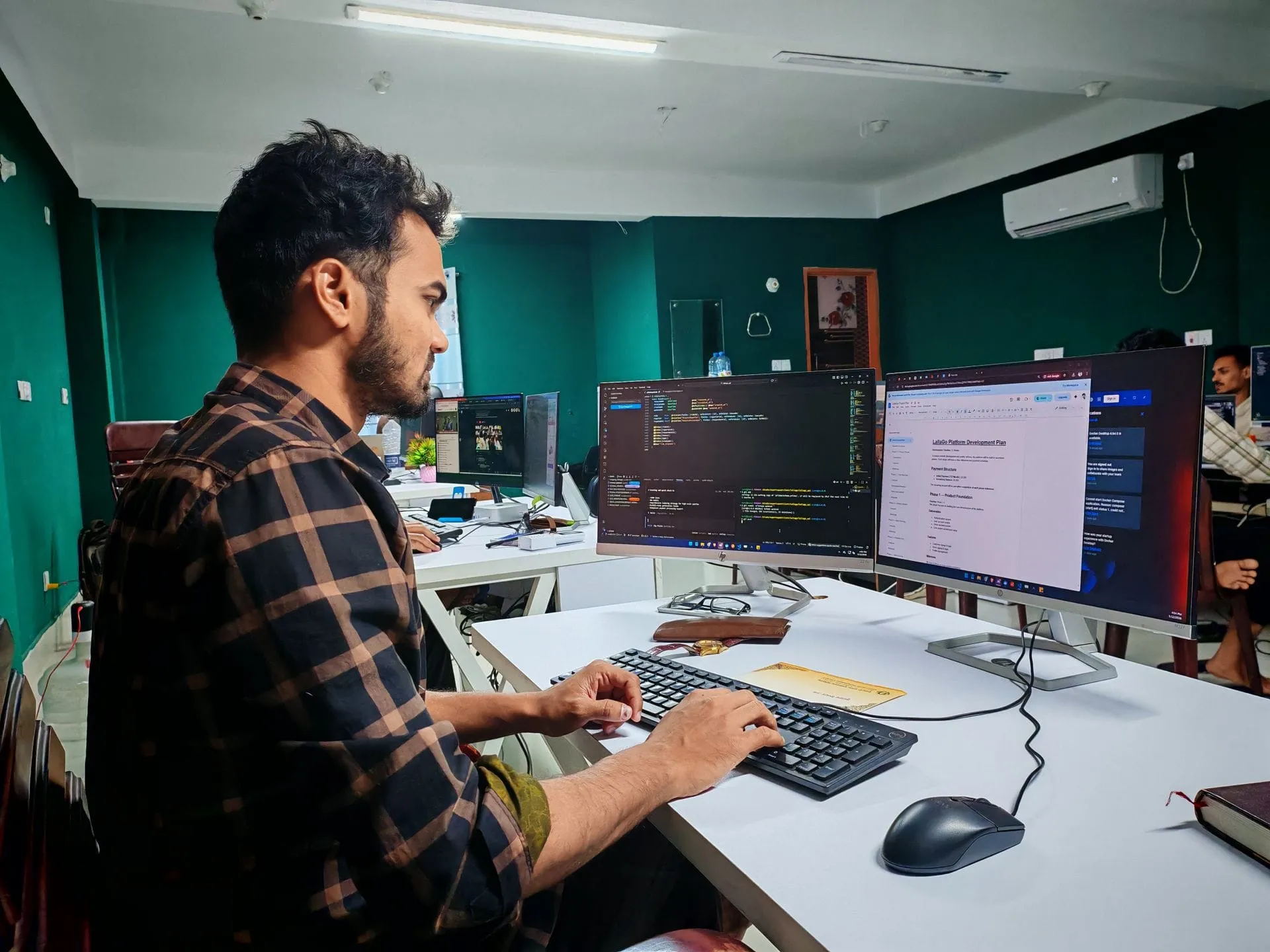 Indian developer working on code across dual monitors in an office